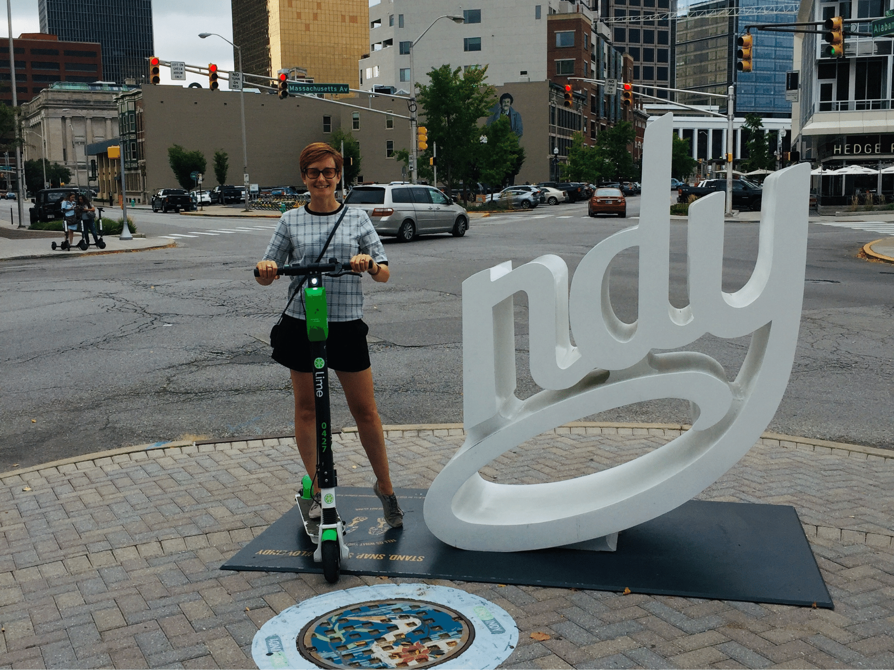 Me standing on a kick-style electric scooter and posing as the "I" in the "Indy" tourism sign in Indiannapolis
