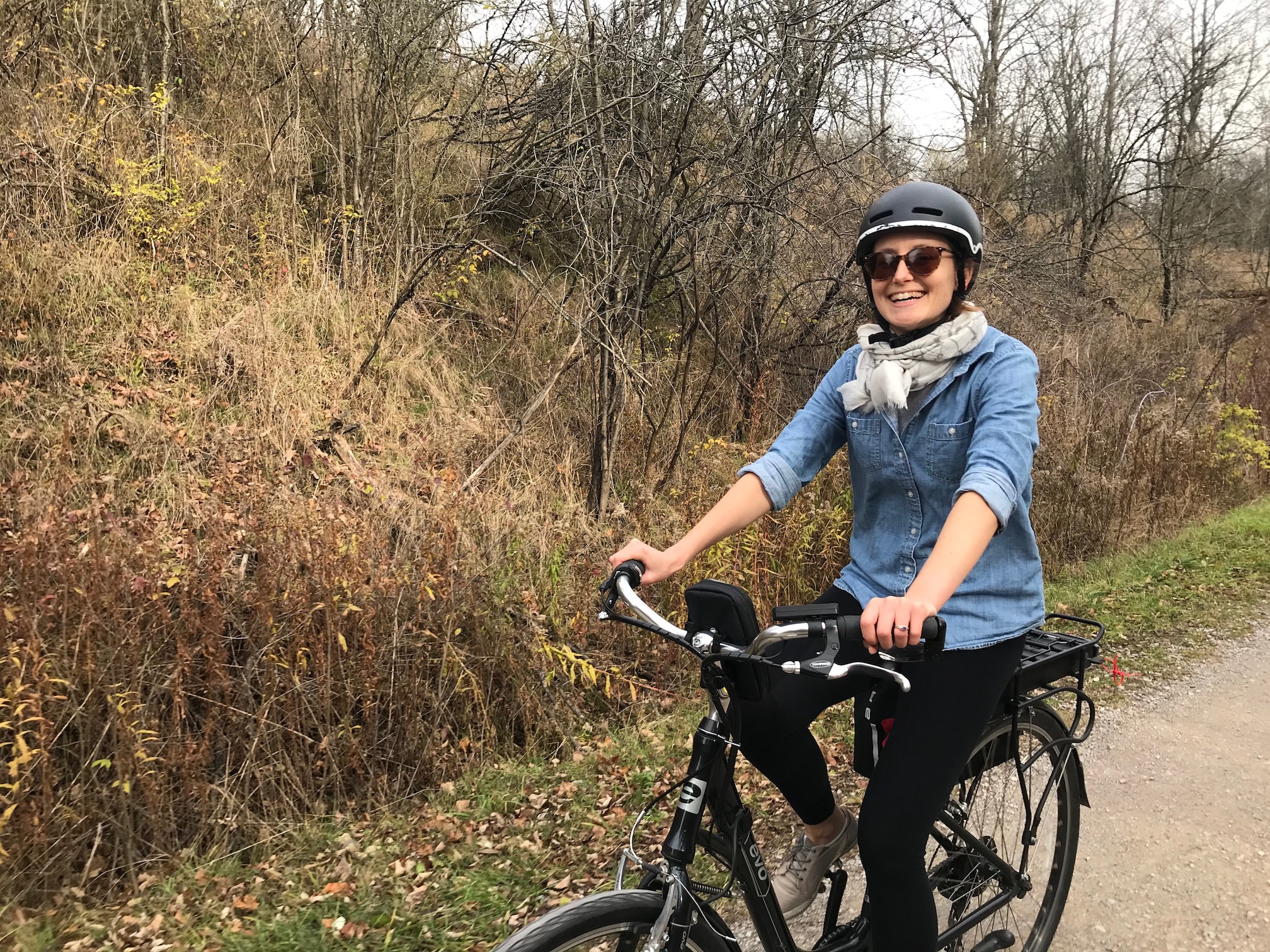 Jamie smiling while riding an electric bicycle on a trail in late Fall