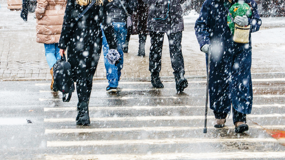 People walking through a crosswalk in the snow, visible from the waist down