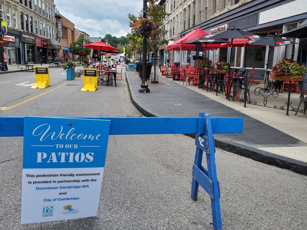 Picture of a street that has been closed to motor vehicle traffic using blue fence posts and that now has restaurant tables on it