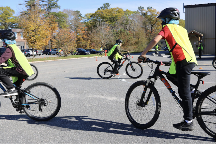 Three students wearing yellow safety vests are riding bicycles in the school yard