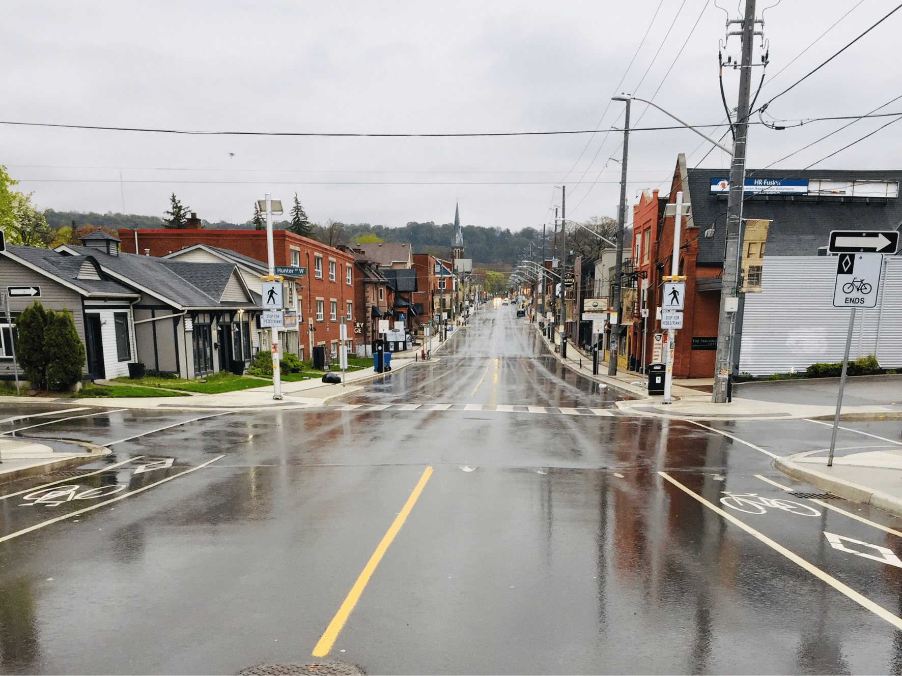 Photo of an empty street in the rain. There are two lanes of motor vehicle traffic, painted bike lanes and sidewalks