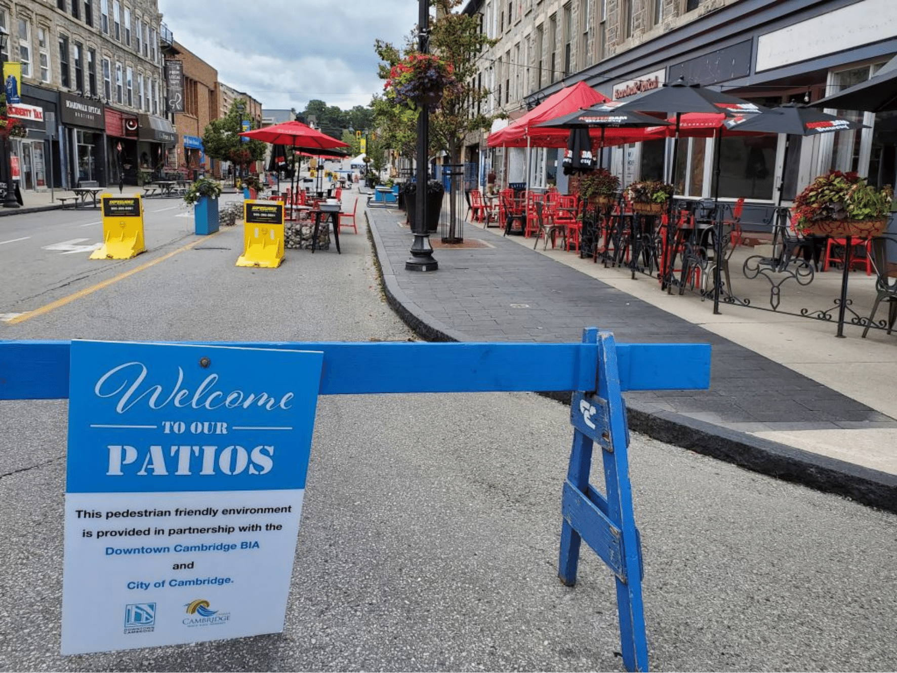 Photo of a street closed to motor vehicle traffic using blue barricades with restaurant patios and red umbrellas on the street and sidewalk